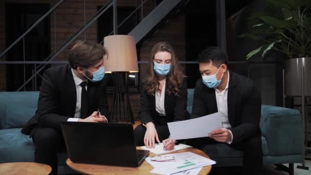 En gruppe multinasjonale forretningsmenn i dress og medisinske masker beslutter å samarbeide internasjonalt om å investere i utviklingen av IT-teknologi under Covid19-pandemien i møterommet.. – stockvideo