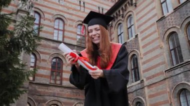 Gecelikli, şapkalı, diplomalı, gülen, dans eden mutlu bir öğrenci..