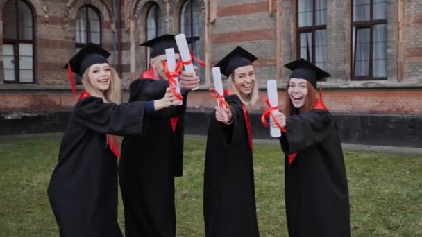 Graduados hombres y mujeres en batas académicas con diplomas en la mano. — Vídeo de stock