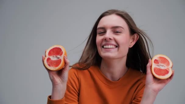 Chica aislada en un fondo gris chica con suéter naranja sostiene pomelo. — Vídeos de Stock