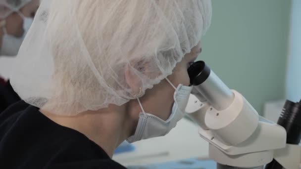 Tıbbi Laboratuvar: Mikroskop kullanarak çalışan Tıbbi Maskeli Doktor. — Stok video