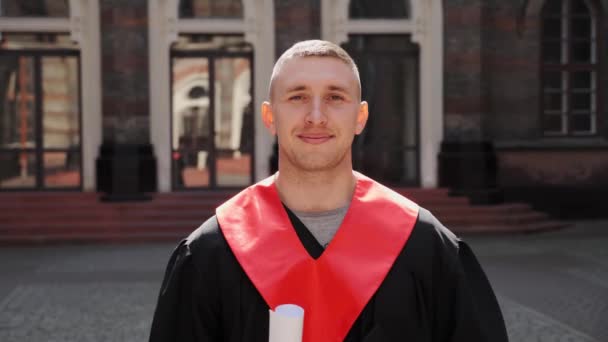 Aantrekkelijke gelukkige afgestudeerde mannelijke student in jurk en hoed met diploma glimlachen. — Stockvideo