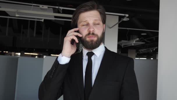 Bonito homem de negócios com barba em um terno clássico conversando com parceiros por telefone em um prédio de escritórios moderno homem alegre ter telefonema no local de trabalho Negócios. Redes sociais. Gente. Aplicações. — Vídeo de Stock