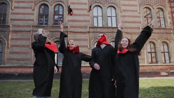 Graduados universitarios en batas de graduación riendo abrazos divertirse graduación. — Vídeo de stock