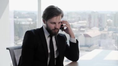 Klasik takım elbiseli yakışıklı bir işadamı, panoramik pencere işinin arka planında, modern bir ofis binasında ortaklarıyla telefonla görüşüyor. Sosyal ağ. - İnsanlar. Uygulamalar.