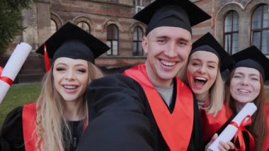 Önlüklü, şapkalı ve diplomalı öğrenciler akademi geçmişinde selfie çekiyorlar..