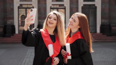 İki kız arkadaş sarışın öğrenci ve önlüklü kızıl saçlı telefon kullanarak selfie çekiyorlar..