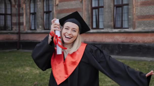 Veselý šťastný absolvent blondýny dívka student v šatech a klobouku držící diplom. — Stock video