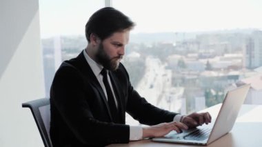 Sakallı, kendine güvenen iş adamı Laptop üzerinde çalışıyor Modern Ofis İş Merkezi 'nde e-posta kontrol ediyor stil sahibi adam önemli bir iş yapıyor büyük pencere arkası iş dünyası sosyal ağı uygulamaları.