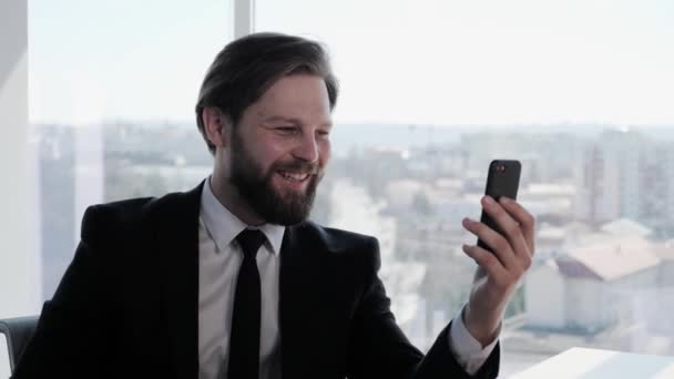 Elegante joven guapo barbudo hombre de negocios con un traje que tiene conferencia de conexión en línea durante la videollamada en la sala de oficina en su lugar de trabajo. Amistosa entrevista a distancia ventana panorámica aplicación. — Vídeo de stock