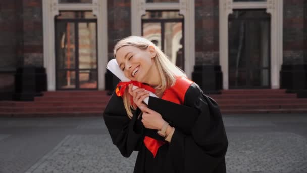 Uteksaminert blond jentestudent i kjole ler og gleder seg til eksamen.. – stockvideo