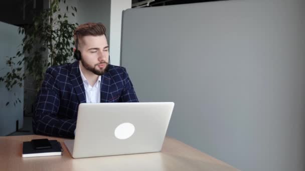 Специалист по технической поддержке мужчина консультирует клиента, бородатого мужчину, в белой рубашке в офисе за ноутбуком в беспроводных наушниках Консультирование людей на горячей линии поддержки пользователей. — стоковое видео