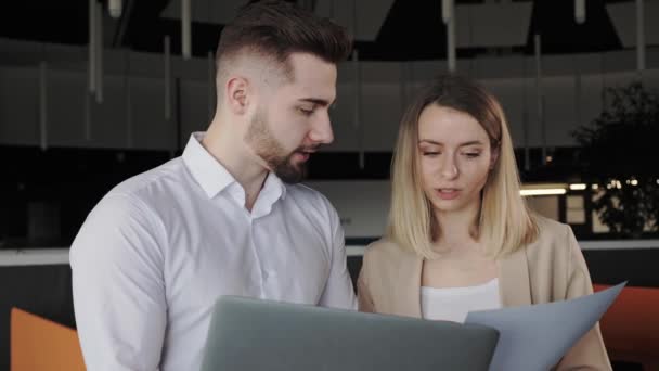 Mannelijke en vrouwelijke collega 's bespreken financiële gegevens analyseren van marketing resultaat in rapport met behulp van documenten die zakelijke gesprekken te helpen collega met corporate project stand in loft office. — Stockvideo