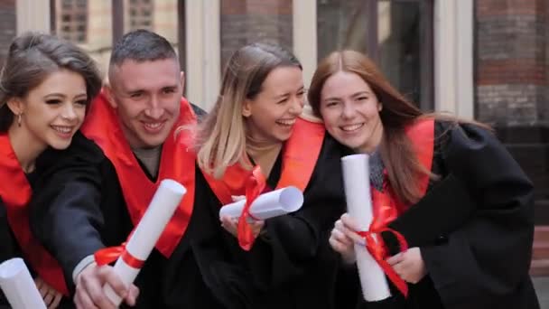 Φοιτητές απόφοιτοι με ακαδημαϊκά φορέματα με διπλώματα στο χέρι ποζάρουν για την κάμερα. — Αρχείο Βίντεο