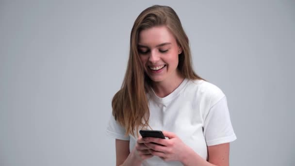 Hermosa mujer aislada en fondo de estudio blanco usando teléfono inteligente en línea. — Vídeos de Stock