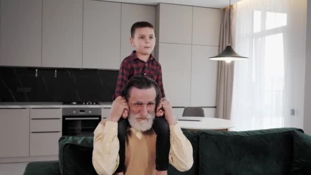 Fröhlicher Großvater mit grauem Bart spielt zu Hause mit einem hübschen Enkel. — Stockvideo