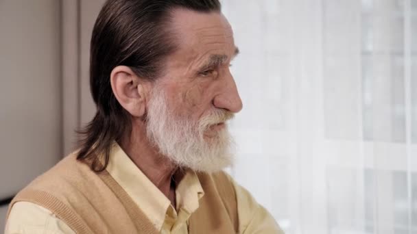 Portret van een oudere oude man met grijze baard hoofd draaien kijkend naar de camera. — Stockvideo