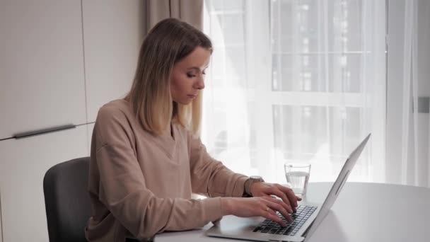 Beautiful blonde woman sitting at home kitchen workplace typing on laptop. — Stock Video