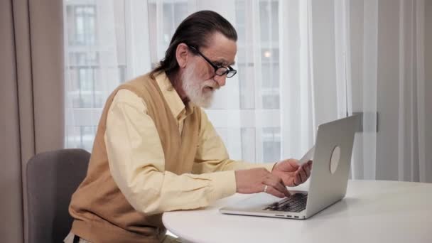 Hombre de edad avanzada mensajes de texto en el ordenador portátil gestionar el papeleo del hogar finanzas documentos. — Vídeo de stock