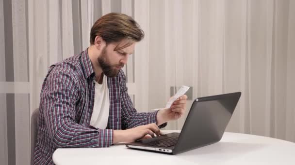 Hombre serio usando calculadora pagando factura en línea sosteniendo papel sentado en casa. — Vídeo de stock