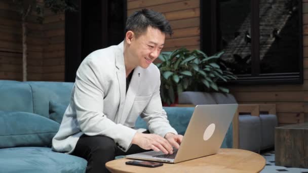 Hombre de negocios chino escribiendo en el ordenador portátil mientras tiene videollamada de negocios. — Vídeo de stock