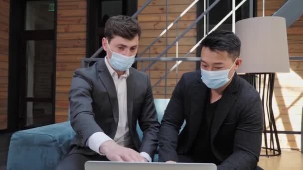 Два транснациональных бизнесмена в медицинской маске обмениваются рукопожатием. — стоковое видео