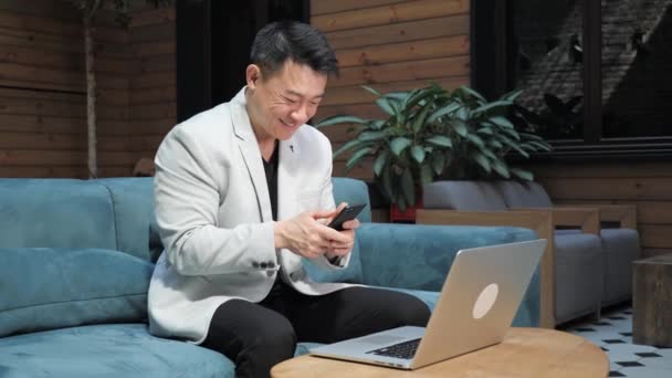 幸せな陽気な中国のビジネスマンは彼のスマートフォンで良いニュースを読んで. — ストック動画
