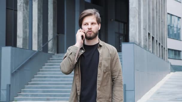 Bell'uomo sta parlando al telefono indossando vestiti casual vicino al centro di coworking. — Video Stock