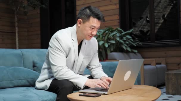 Selvsikker asiatisk forretningsmand skriver på laptop tastatur i hyggeligt loft kontor. – Stock-video