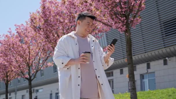 Корейський чоловік Чатінг на Смартфоні на задньому плані прекрасних дерев. — стокове відео
