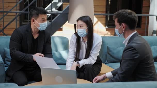 Et team med multinasjonale, asiatiske forretningsmenn i medisinske masker som ser på presentasjon – stockvideo