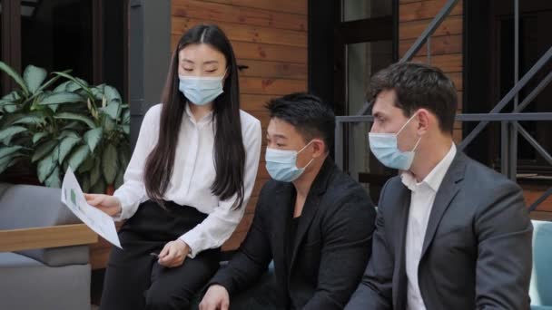Kinesisk kvinne som viser forretningsplan for diverse kolleger i beskyttelsesmasker. – stockvideo