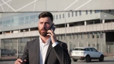 Genç iş adamı elinde akıllı telefonuyla sokaklarda yürüyor iş görüşmeleri yapıyor.