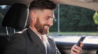Neşeli yönetici arabada otururken akıllı telefon kullanarak sohbet ediyor..