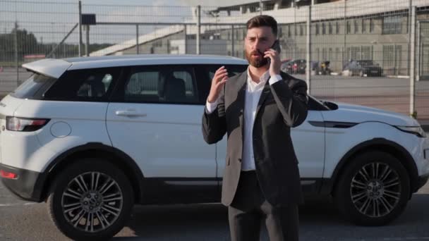 Empresário barbudo usando smartphone conversando com parceiros perto de carro branco moderno — Vídeo de Stock