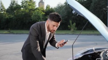 Genç üzgün adam kaputu açık kırık arabanın yanında duruyor..