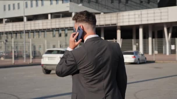 Back view of young businessman is talking on smartphone przejdź do nowoczesnego samochodu. — Wideo stockowe