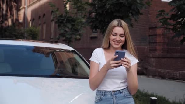 젊은 금발의 여인 이 백 차 가까이에 서 있다. 현대 휴대 전화를 사용 함. — 비디오