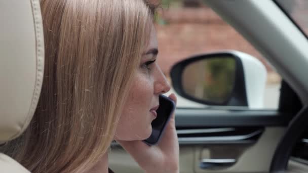 Schöne blonde Mädchen mit Sommersprossen sitzt in einem Luxusauto und benutzt Mobiltelefon. — Stockvideo