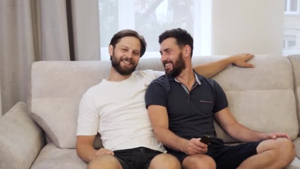 Amando o mesmo sexo casal masculino abraçando como eles se deitam no sofá em casa assistindo TV. — Vídeo de Stock