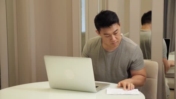 Серьезный азиатский бухгалтер-мужчина, сидящий в домашнем офисе, работает дистанционно. — стоковое видео