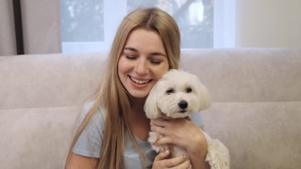 Leende ung blond kvinna kramas med sällskapsdjur hund sitter på soffan. — Stockvideo
