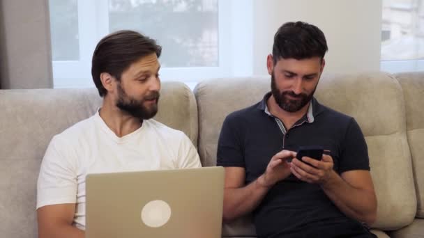 Joven pareja del mismo sexo sentada en el sofá en casa usando juegos de tecnología. — Vídeos de Stock