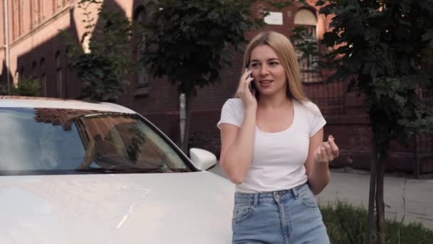 Joven hermosa chica con pecas hablando por teléfono cerca de coche blanco moderno. — Vídeos de Stock