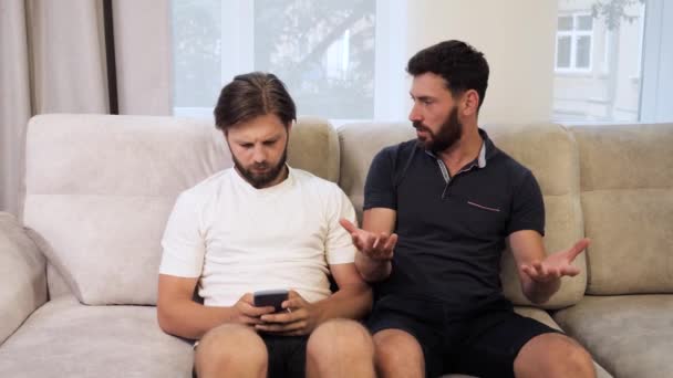 소파에 앉아서 휴대폰 충돌 장면을 보고 있는 동성애자 커플. — 비디오