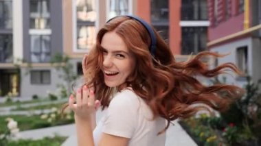 Kızıl kıvırcık saçlı güzel, genç bir kadın açık havada müzik dinliyor..