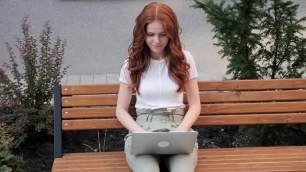 Felice ragazza dai capelli rossi freelance che lavora su un computer portatile in un parco. — Video Stock