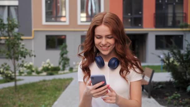 Piękna dziewczyna stojąca w dzielnicy miasta, słuchając muzyki wpisując Wiadomość. — Wideo stockowe