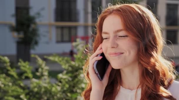 Joyeux rousse jolie fille avec des taches de rousseur parler par téléphone mobile fond de la ville. — Video