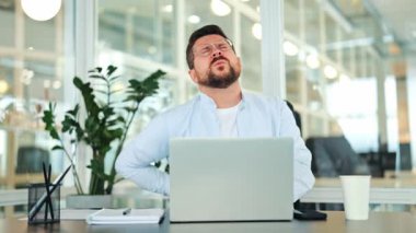 Açık mavi bir gömlek giyen yorgun işadamı modern bir ofis masasında otururken sırt ağrısı çekiyor. Rahatsızlık ve yorgunluk hissediyor..